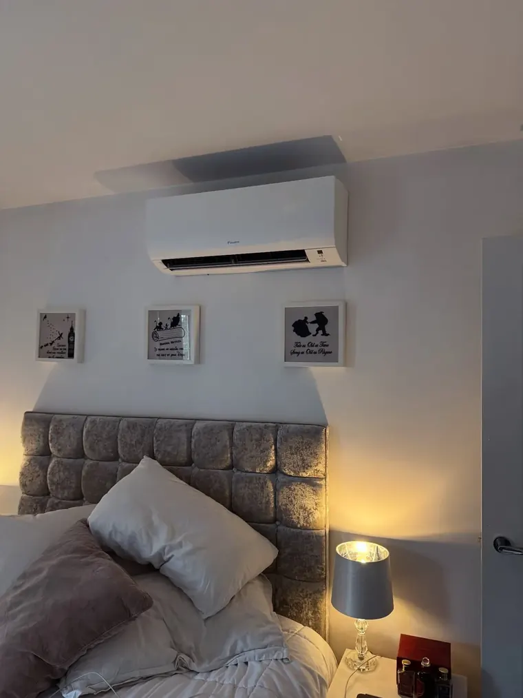 Wall-mounted air conditioning unit above a bed in a finished bedroom