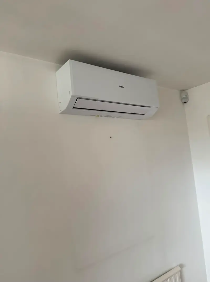 Wall-mounted air conditioning unit fitted high on a plain wall