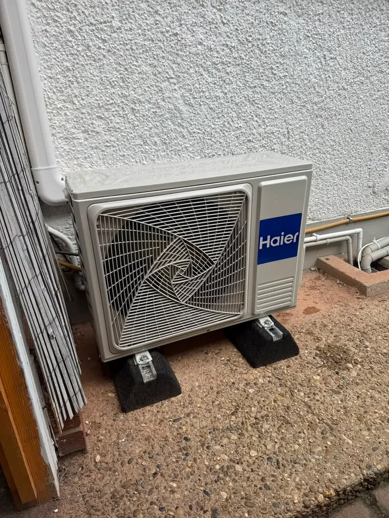 Haier condenser unit sat on feet beside an external wall