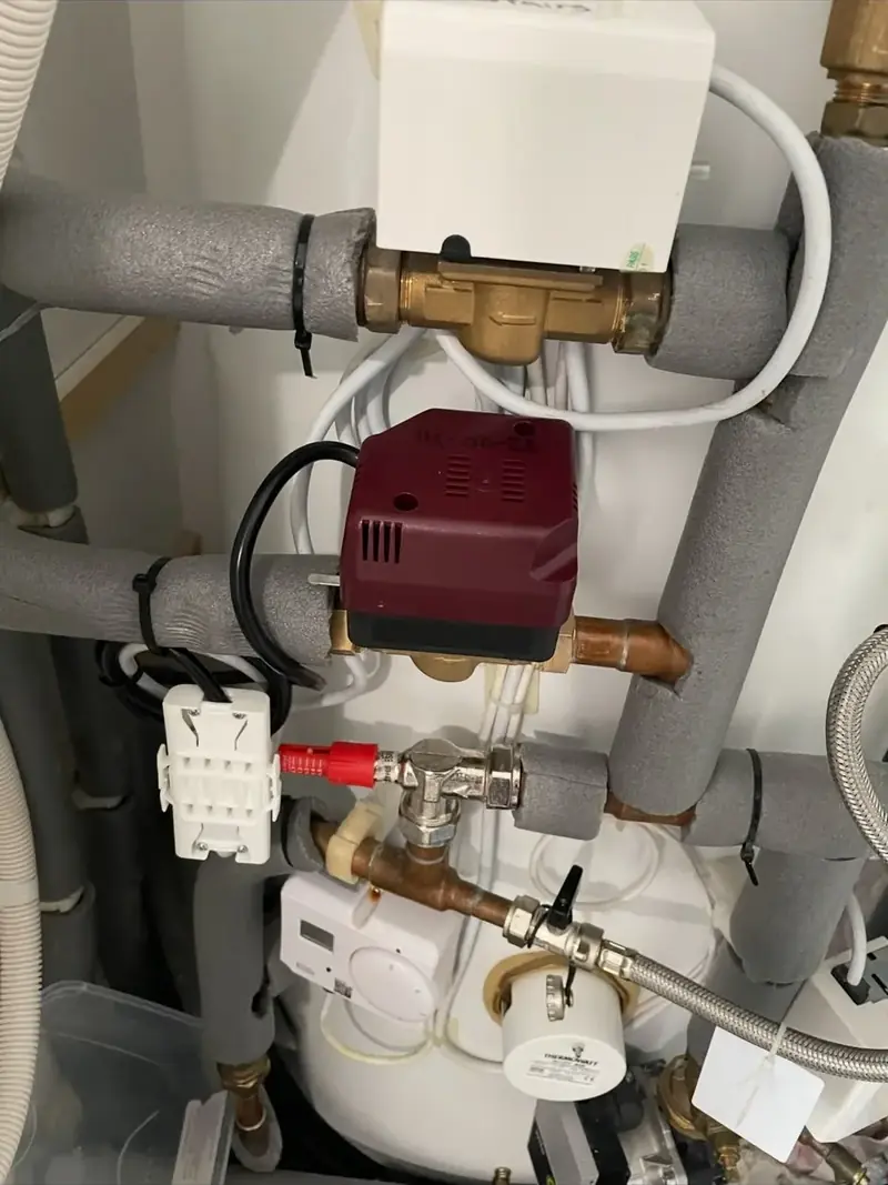 Motorised zone valves and insulated pipework above a hot water cylinder