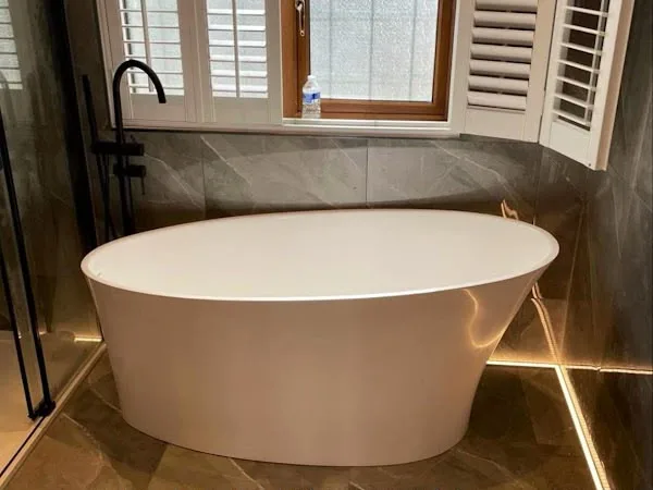 A finished bathroom with a freestanding bath, dark tiling and shutters