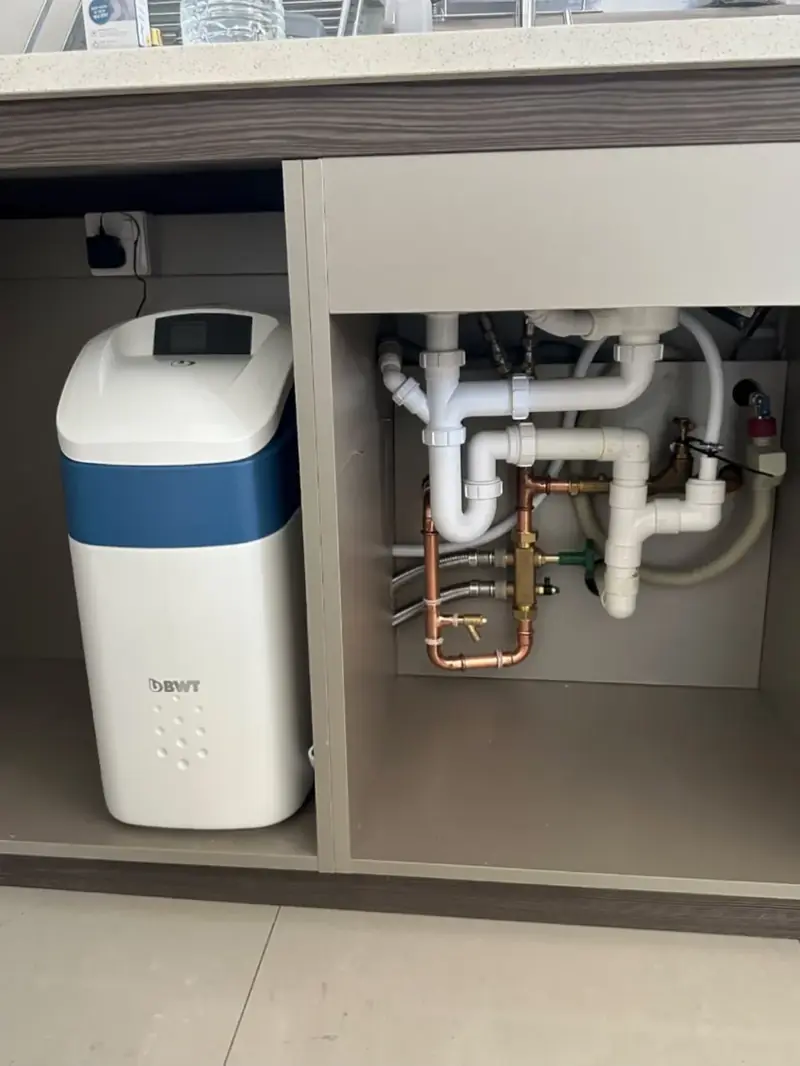 Water softener fitted under a kitchen counter beside the finished pipework
